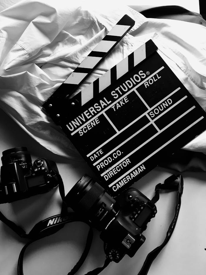 about-us Black and white photo of a film clapperboard and cameras on a white surface.