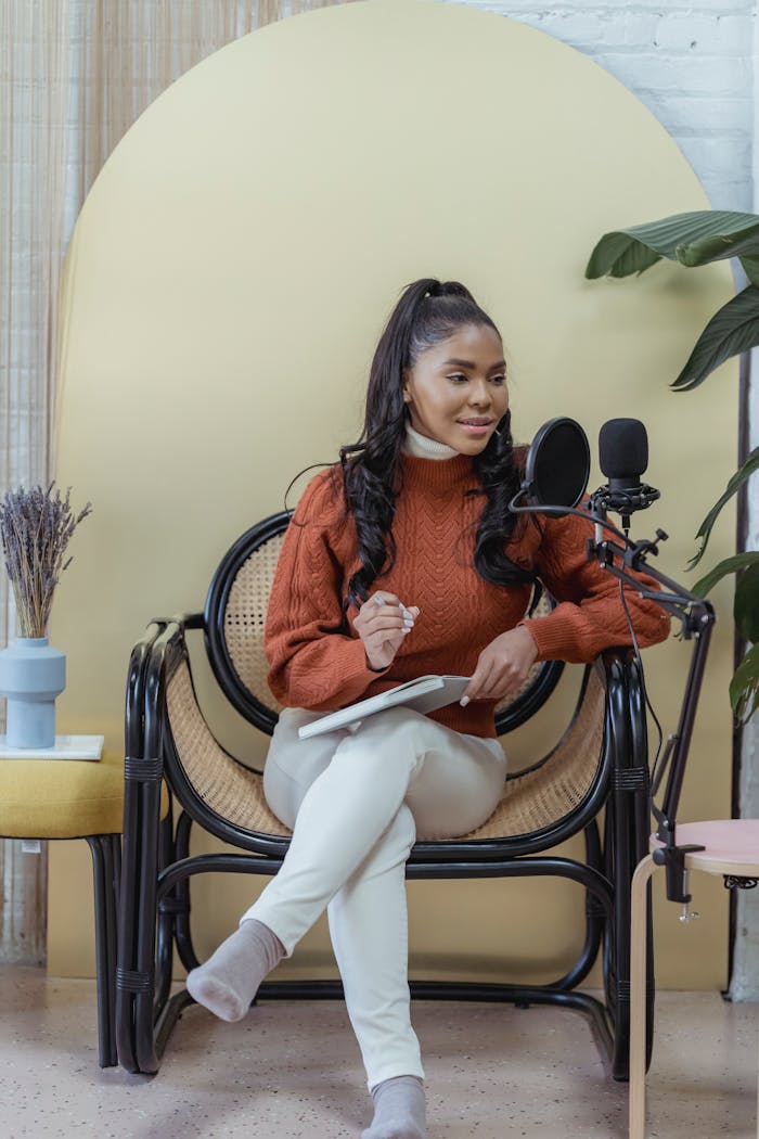 who-we-are A young woman sits in a stylish home studio, recording a podcast with a microphone.